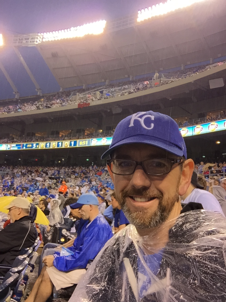 Man wearing a KC hat and rain slicker in a stadium.